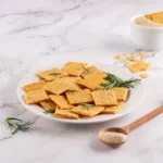 Cream cracker caseiro crocante INGREDIENTES • 40 g de sementes de chia • 100 g de flocos de aveia sem glúten • 120 ml de água PREPARO • O primeiro passo é hidratar a chia. Coloque as sementes em uma tigela, adicione a água e misture bem. Depois, deixe descansar por cerca de 10 a 15 minutos, até formar um gel natural. • Esse processo é importante porque a chia funciona como substituta do ovo, ajudando a dar liga à massa. • Em seguida, acrescente os flocos de aveia sem glúten e misture até obter uma massa consistente e moldável. Se necessário, utilize as mãos para incorporar melhor os ingredientes. • Abra a massa entre duas folhas de papel manteiga com a ajuda de um rolo. O ideal é deixar a espessura bem fina para garantir um resultado mais crocante após assar. • Depois, corte os biscoitos em retângulos ou quadrados, no estilo tradicional do cream cracker. • Leve ao forno preaquecido a 180°C por aproximadamente 15 a 25 minutos, até dourar. O tempo pode variar conforme a potência do forno, então vale acompanhar nos minutos finais para evitar que os biscoitos queimem.